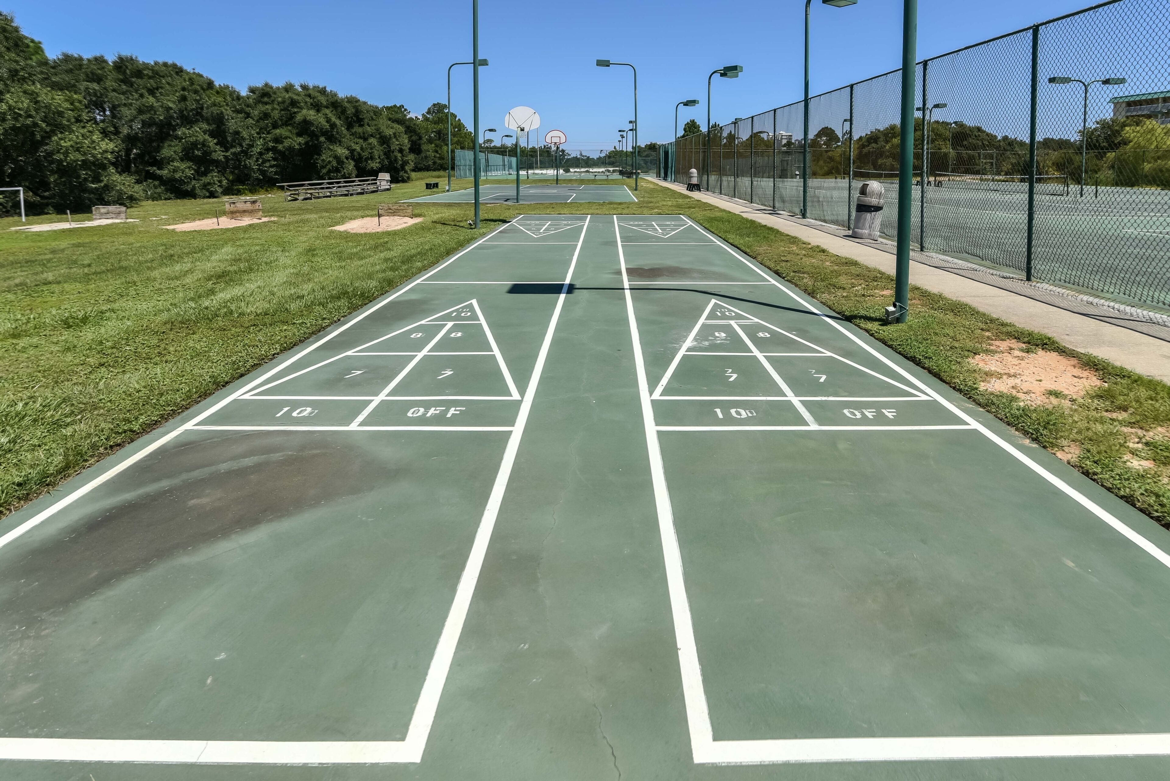 Un campo da shuffleboard con segnalature verdi e numeri, circondato da una recinzione e alberi.