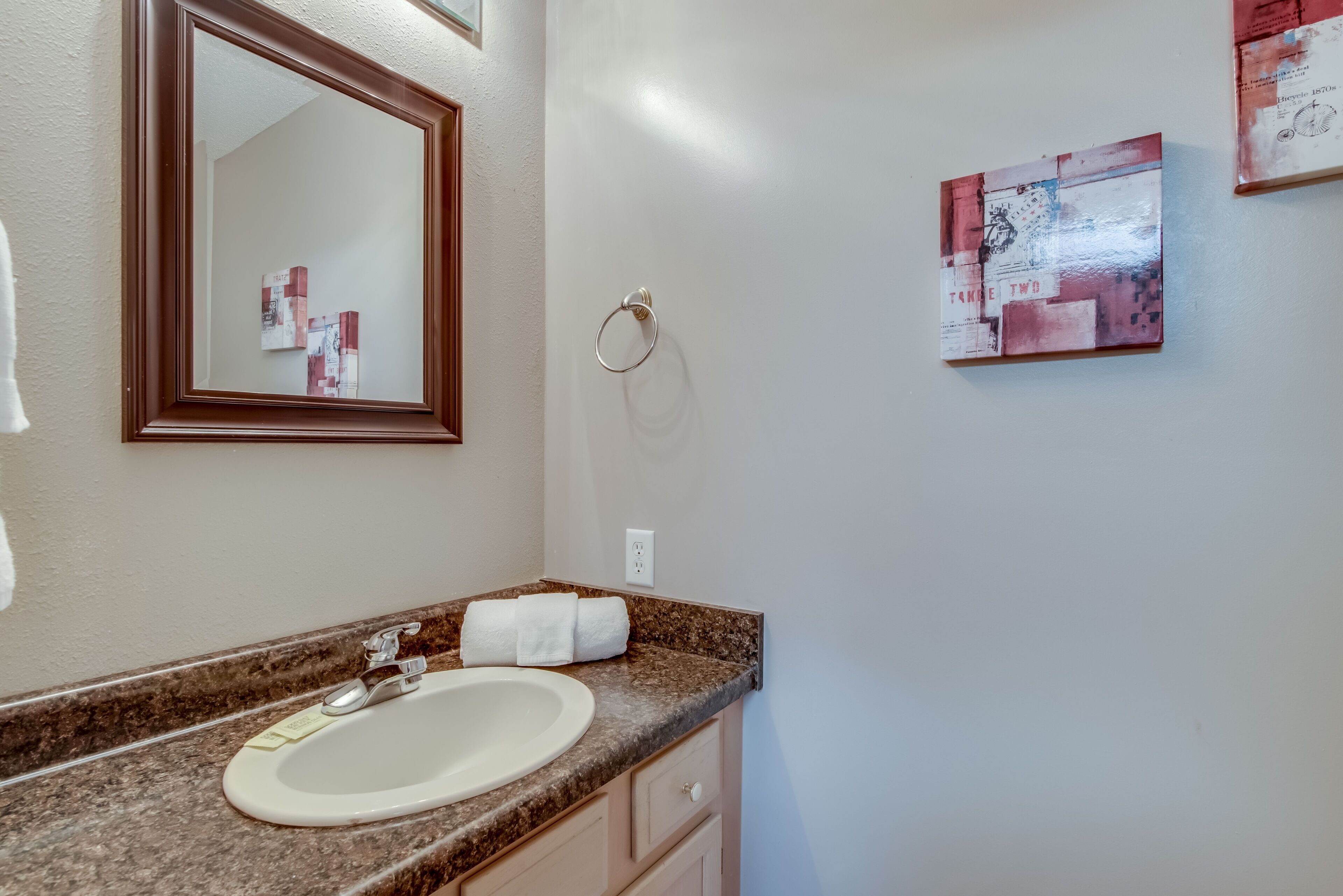 A bathroom with a granite countertop, a white sink, a mirror, and a towel rack.