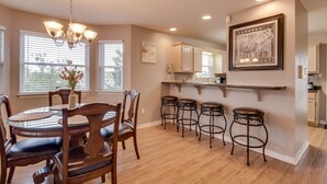 A dining area with a round table, four chairs, and a chandelier. There are four stools against the wall. - Summer Palace B 2 Bedroom Duplex by RedAwning (Gulf Shores)