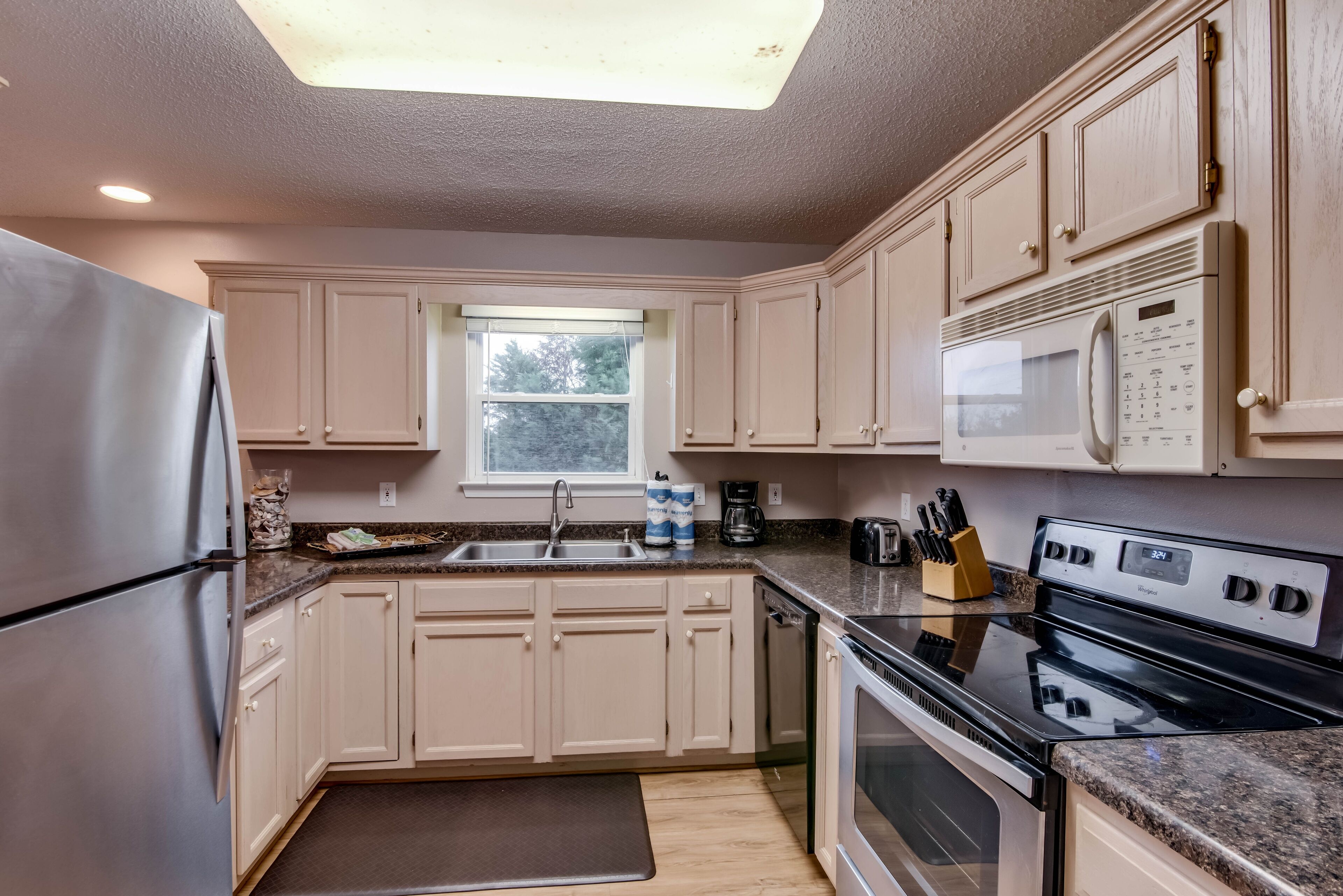 A kitchen with beige cabinets, stainless steel appliances, a window, and a skylight.