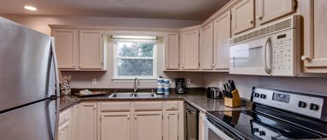 A kitchen with beige cabinets, stainless steel appliances, a window, and a skylight.