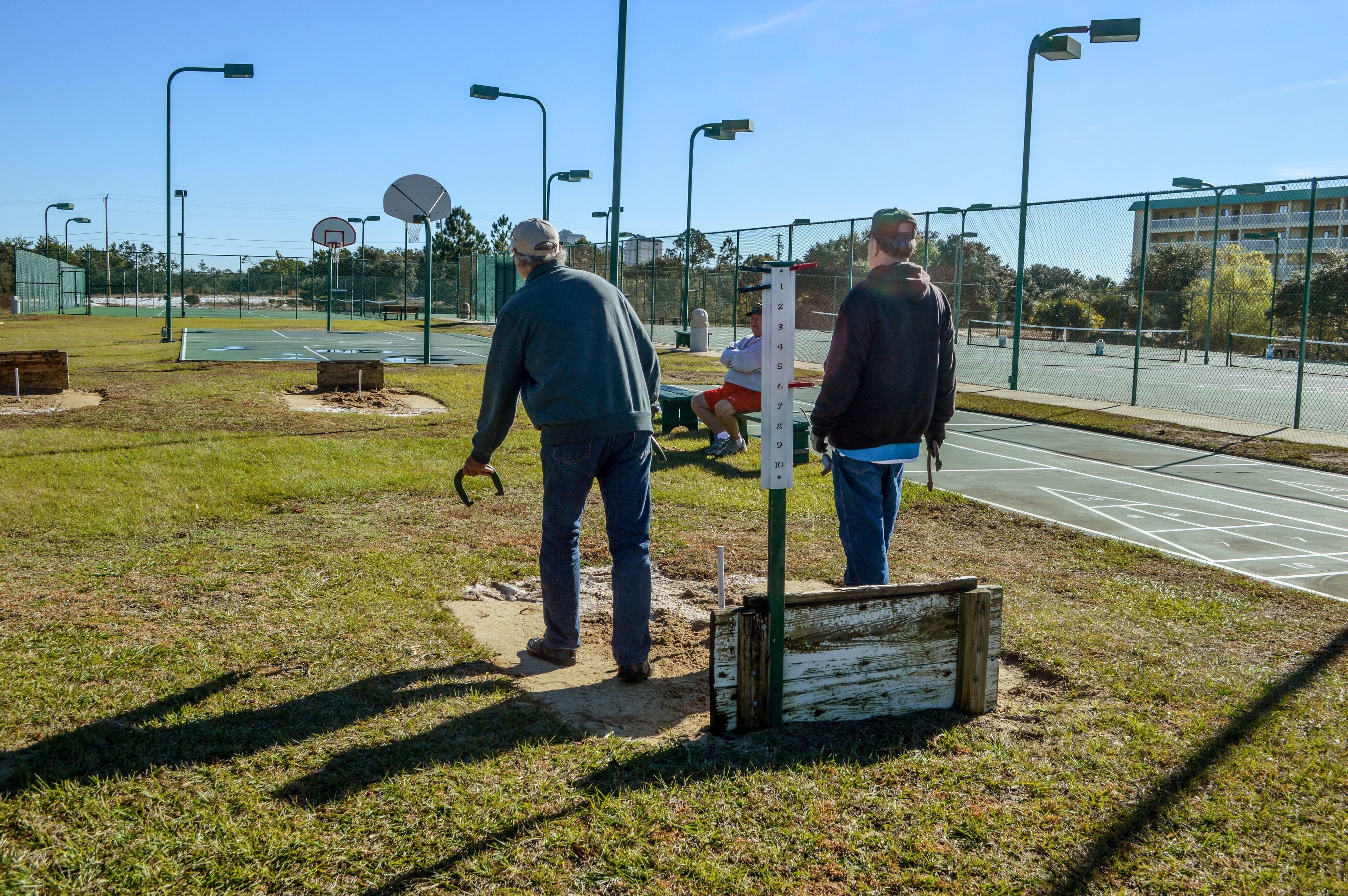 An outdoor basketball court with a fence, street lamps, and a basketball hoop.