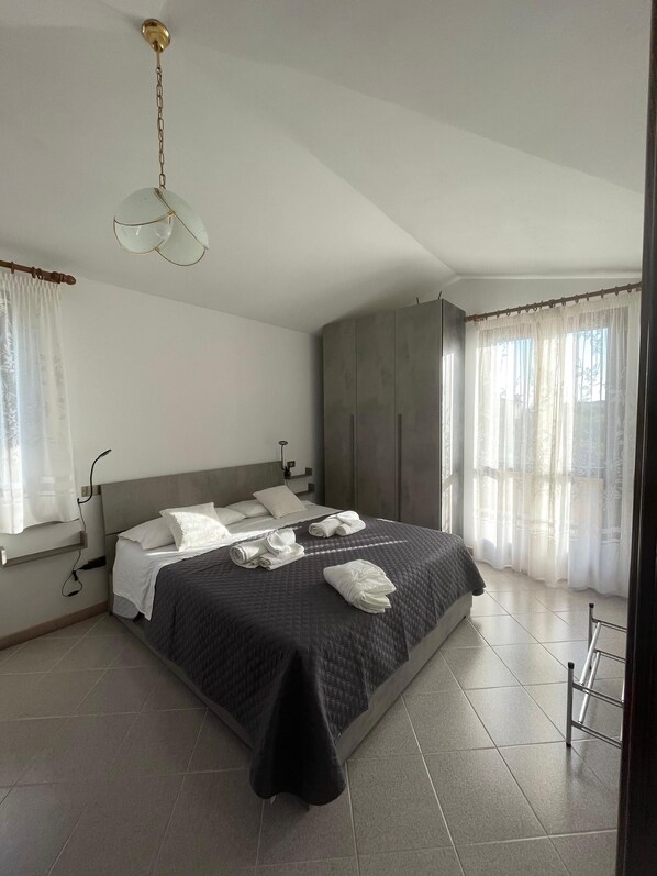 A neatly made bed with pillows and towels, a ceiling fan, and a window with sheer curtains.