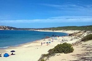 A beach with tents and people, clear skies, and calm water.