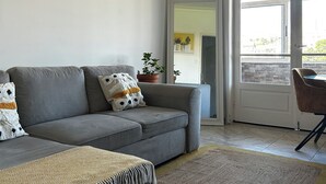 A living room with a grey sofa, a patterned throw blanket, a woven rug, and a ceiling light fixture.