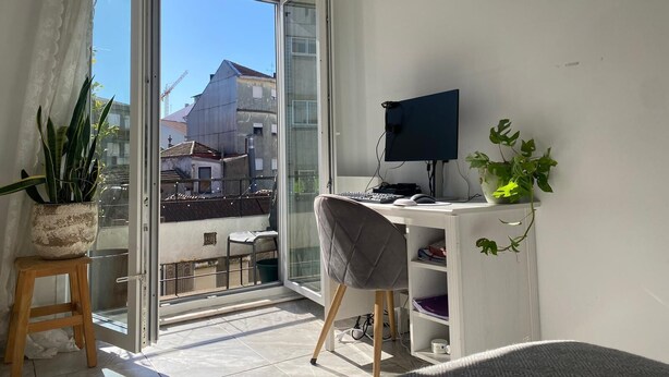 A balcony with a desk, chair, computer, and potted plants.