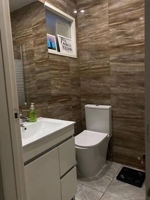 Une salle de bain moderne avec un lavabo, des toilettes et un meuble-lavabo blancs. Deux citations inspirantes encadrées sont accrochées au mur.