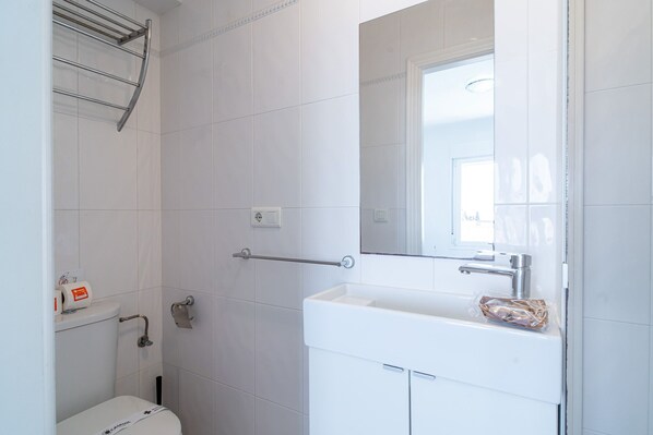 Une salle de bain avec un lavabo blanc, un miroir, un porte-serviettes et des toilettes.