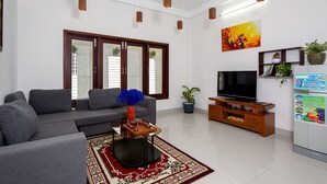 A modern living room with a grey sofa, a coffee table with decorative items, a flat-screen TV, and a refrigerator with magnets.