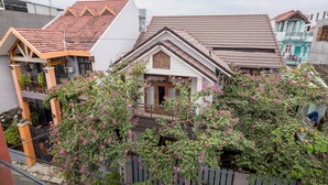 A residential building with a sloped roof, a balcony, and a garden with flowering plants.