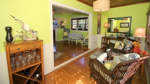 Une pièce avec un plancher en bois, un canapé en osier, un coin repas avec une table et des chaises, et un miroir au mur.