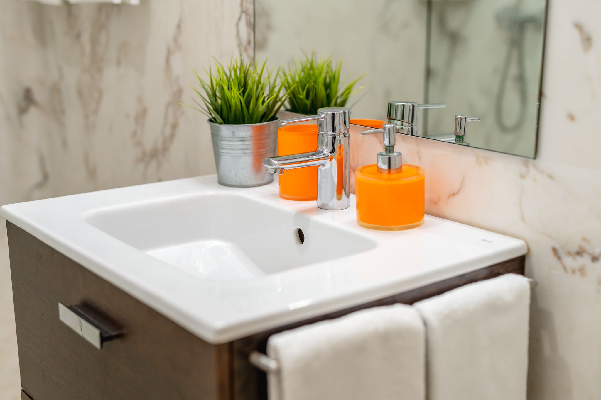 Une salle de bain avec un lavabo blanc, deux distributeurs de savon orange et une plante en pot.
