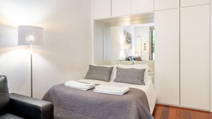 Quarto de hotel moderno com cama, poltrona, luminária e armário.