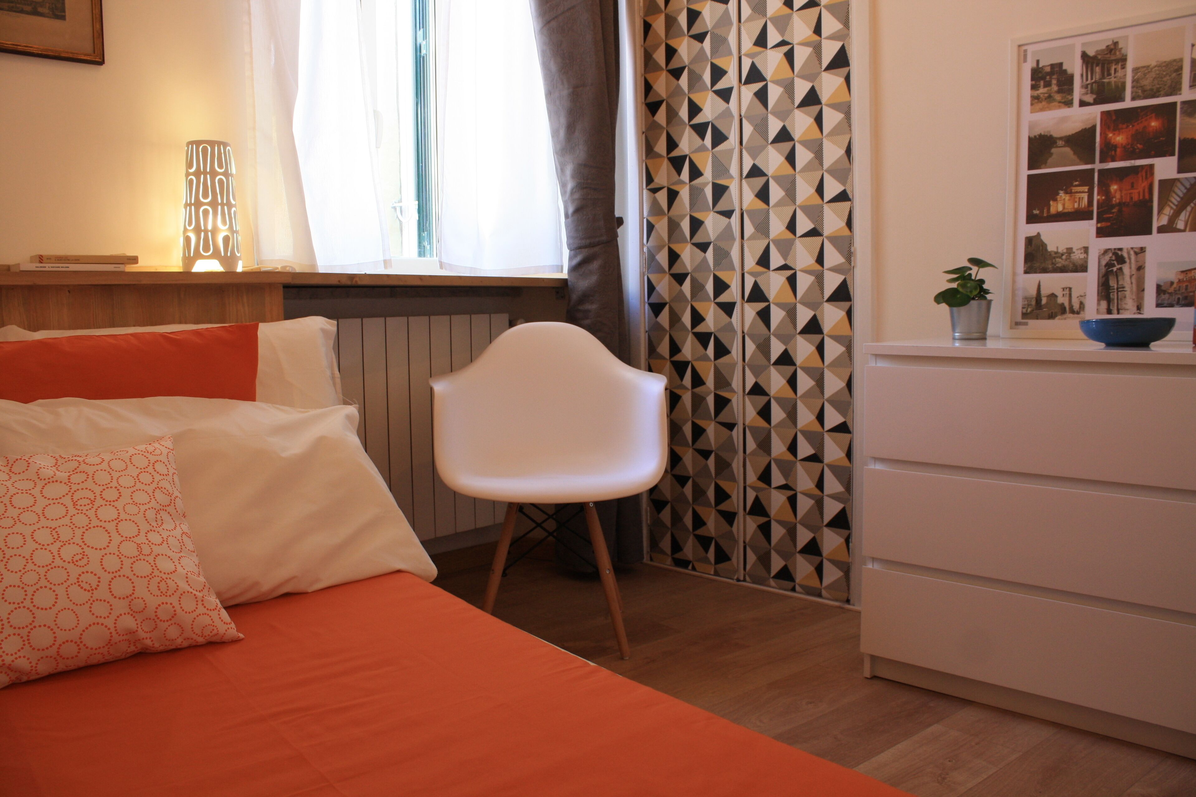 Une chambre à coucher avec un lit, des oreillers, une chaise, une commode et une fenêtre avec des rideaux.