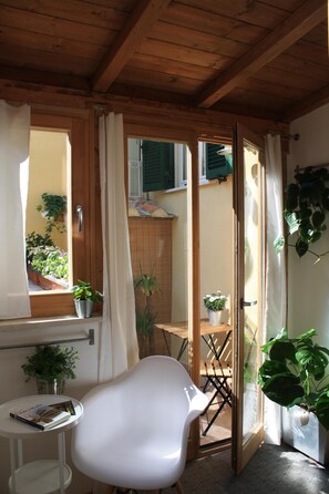 A room with a wooden ceiling, a white chair, a small table with a book, and potted plants.