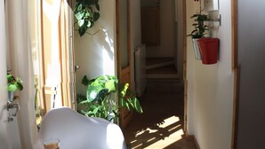 A narrow hallway with wooden beams, a white chair, a small table with a book and a glass, and potted plants. - house in the medieval district of Tivoli (Tivoli)