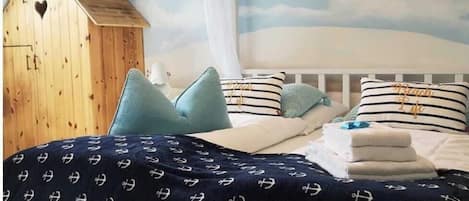 Un dormitorio con cama, almohadas, dosel, estructura de madera que recuerda a un granero, y un mural en la pared con nubes y cielo.
