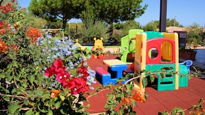 Zona de juegos infantiles con estructuras de plástico de colores y diversas flores en primer plano.