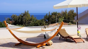 Una hamaca y una silla de descanso en un patio con suelo de baldosas y vistas al mar.