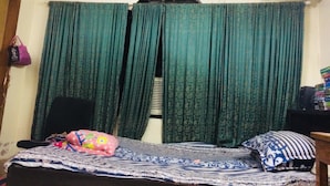 A small room with a bed, a chair, a desk with a computer, and a window with green curtains. - Redwan's home (Dhaka)