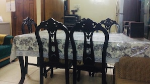 A dining area with a table covered by a patterned tablecloth, surrounded by ornate chairs. - Redwan's home (Dhaka)