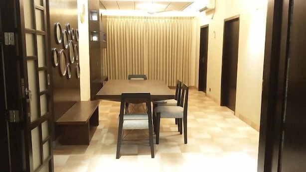 A dining area with a large table, chairs, and a bench. There are curtains and a door in the background. - Redwan's home (Dhaka)