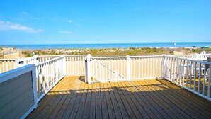 Een houten terras met witte hekwerken met uitzicht op een strand.