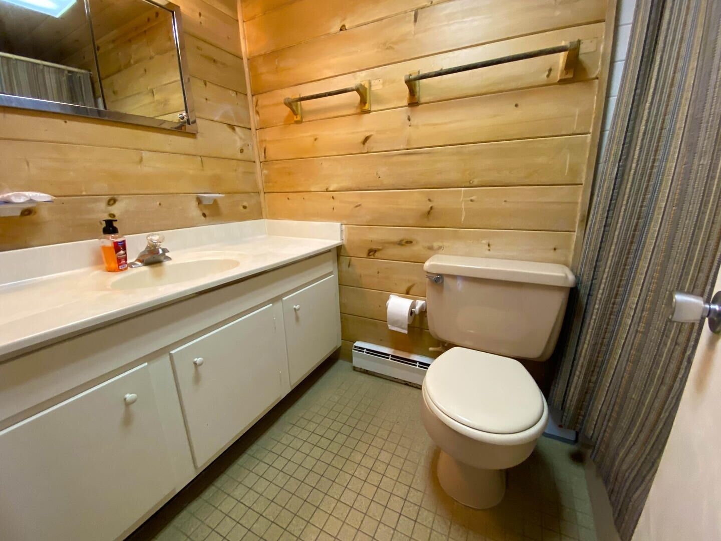 Un baño con paredes de madera, un lavamanos blanco, un inodoro y un espejo.