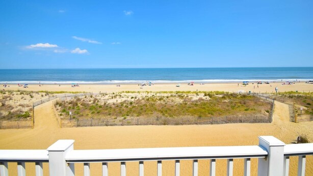 Een strand met een zandpad en een houten omheining.