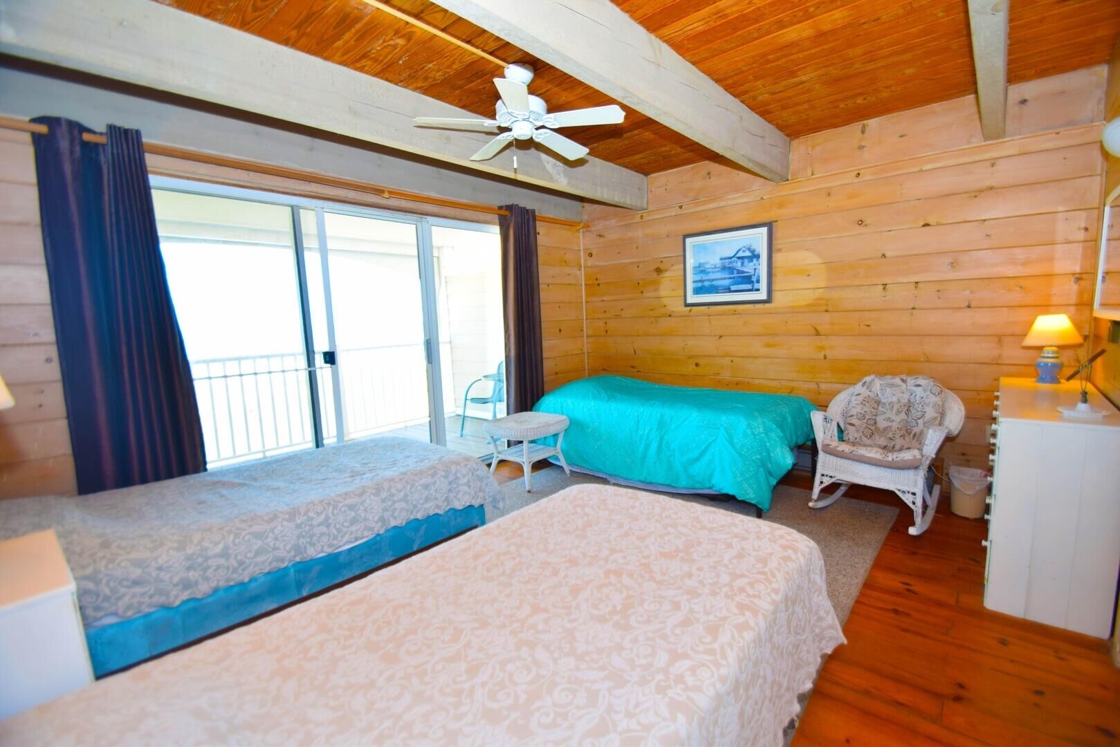 A cabin with two beds, a ceiling fan, a chair, a desk, and a window with curtains.