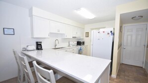 Une cuisine avec des meubles blancs, un îlot central doté de chaises, un réfrigérateur et un four à micro-ondes.