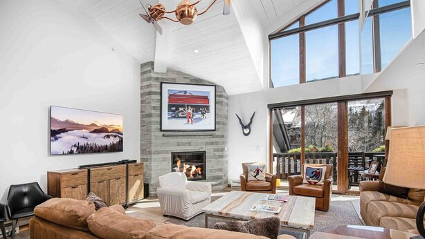 A spacious living room with a fireplace, large windows, and a high ceiling. - Ge Inn Plaza #109 4 Bedroom Condo by RedAwning (Vail)