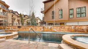 A pool area with a stone wall, a hot tub, and a staircase leading to a building with balconies. - Ge Inn Plaza #109 4 Bedroom Condo by RedAwning (Vail)