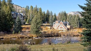Une grande maison située en bord de rivière, entourée d’arbres et de montagnes.