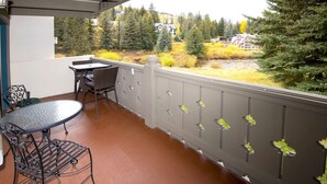 Un balcon avec une table et des chaises, donnant sur une zone boisée où l’on aperçoit des maisons au loin.