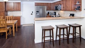 Une cuisine dotée de meubles en bois, d’un réfrigérateur en acier inoxydable, d’un four à micro-ondes et d’un four encastré. On y trouve également une table à manger en bois, des chaises et deux tabourets de bar.