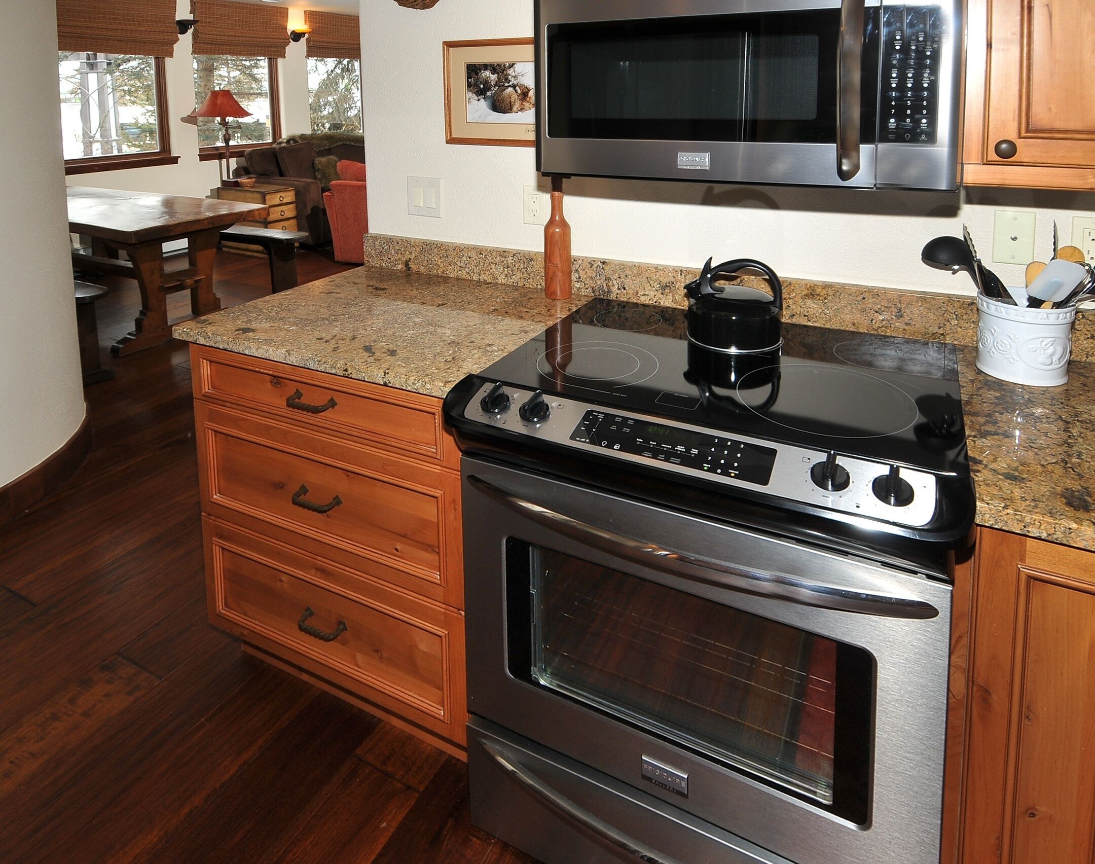 A kitchen with a stainless steel stove, oven, and microwave. There is a wooden cabinet with drawers and a granite countertop.