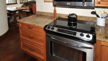A kitchen with a stainless steel stove, oven, and microwave. There is a wooden cabinet with drawers and a granite countertop.