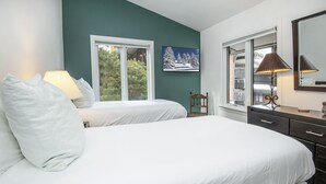 A bedroom with two beds, a dresser, a chair, and a window with a view of trees.