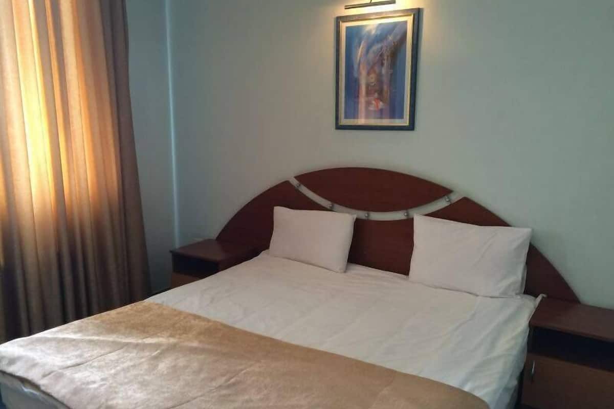 A hotel room with a bed, nightstands, a painting on the wall, and a window with curtains.