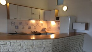 Una cucina con isola in pietra, mobili bianchi, un forno a microonde e un forno da incasso.
