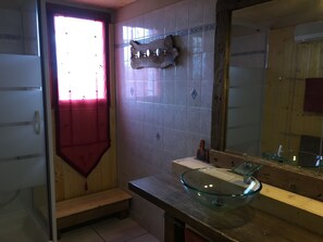 Ein Badezimmer mit einem Glaskonstruktion-Waschbecken, einer Holzbodenbank, gefliesten Wänden und einem Spiegel.