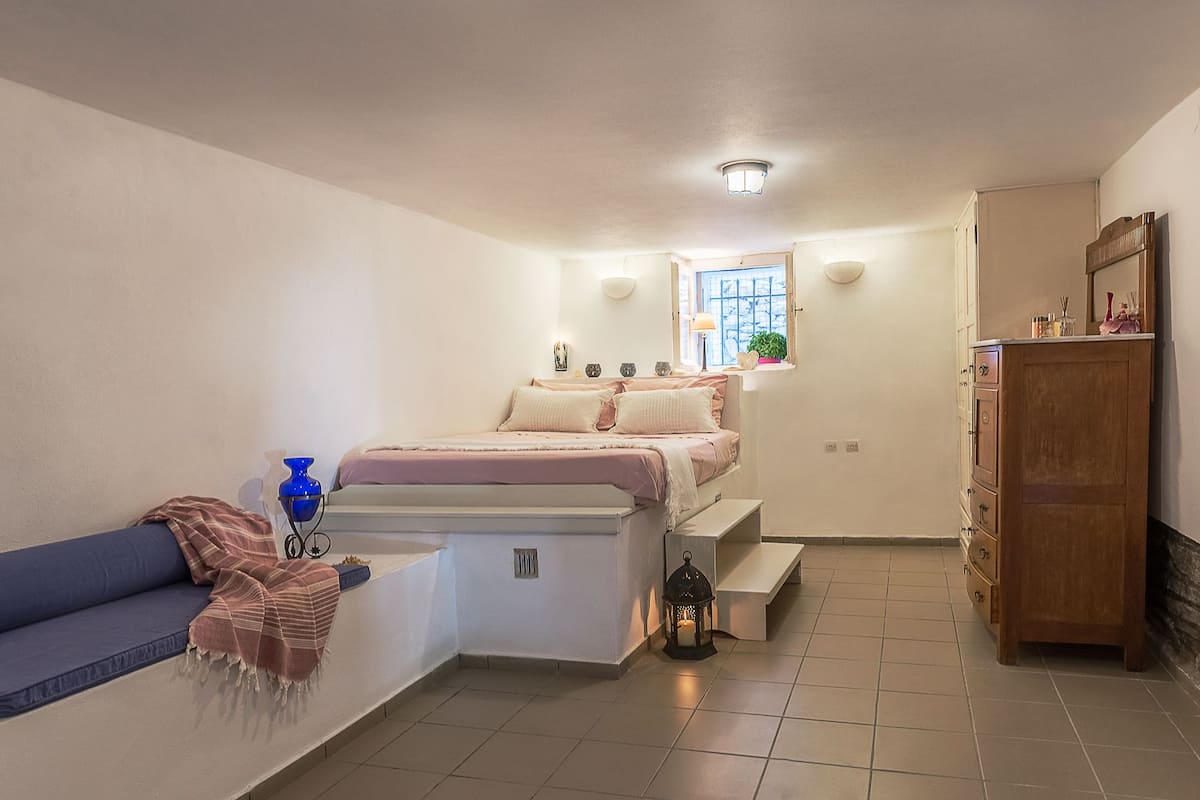 A compact bedroom with a bed, a small window, a nightstand, a cabinet, and a blue chair.