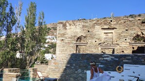 A stone pool with a clear blue water, surrounded by stone walls and a white building in the background.