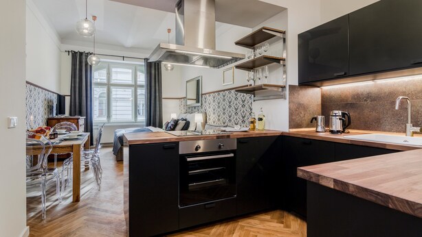 A modern kitchen with black cabinets, a wooden countertop, and a built-in oven. - PRG Trendy Central APT by Michal&Friends (Prague)