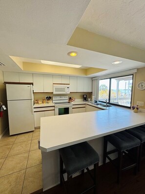 A modern kitchen with a central island, white cabinetry, a microwave, and a refrigerator.