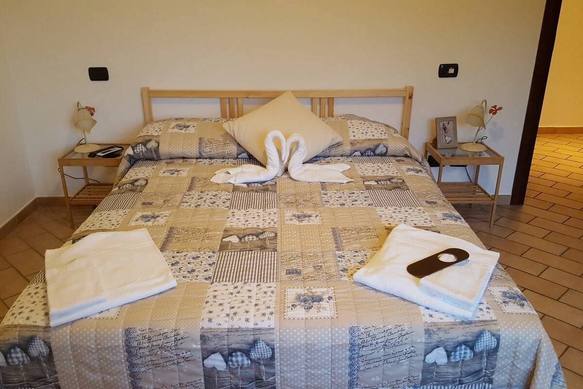 Una cama bien hecha con colcha, almohadas y toallas ordenadas.