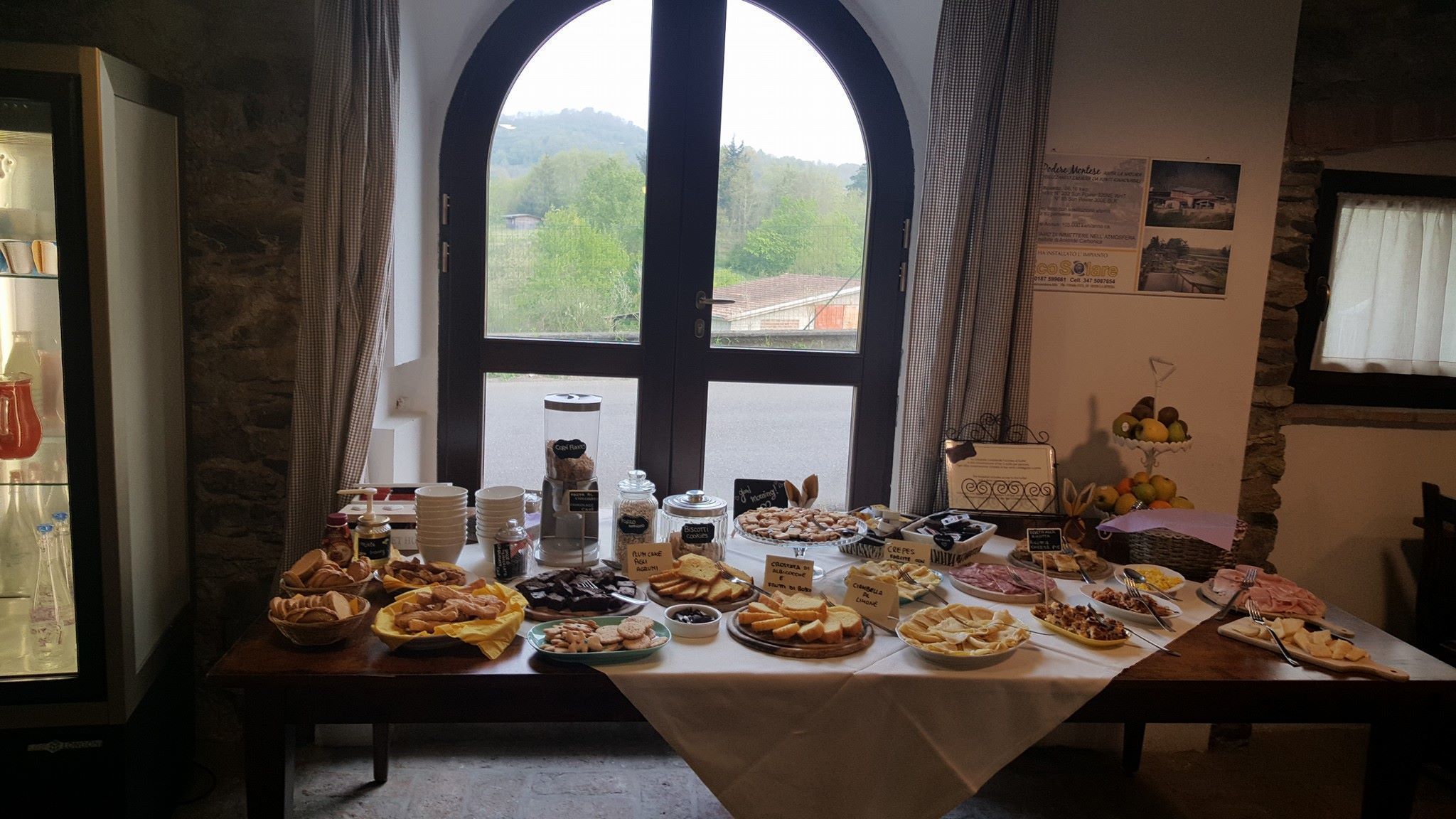 A breakfast buffet with various pastries, fruits, and beverages on a table in a room with a large arched window.