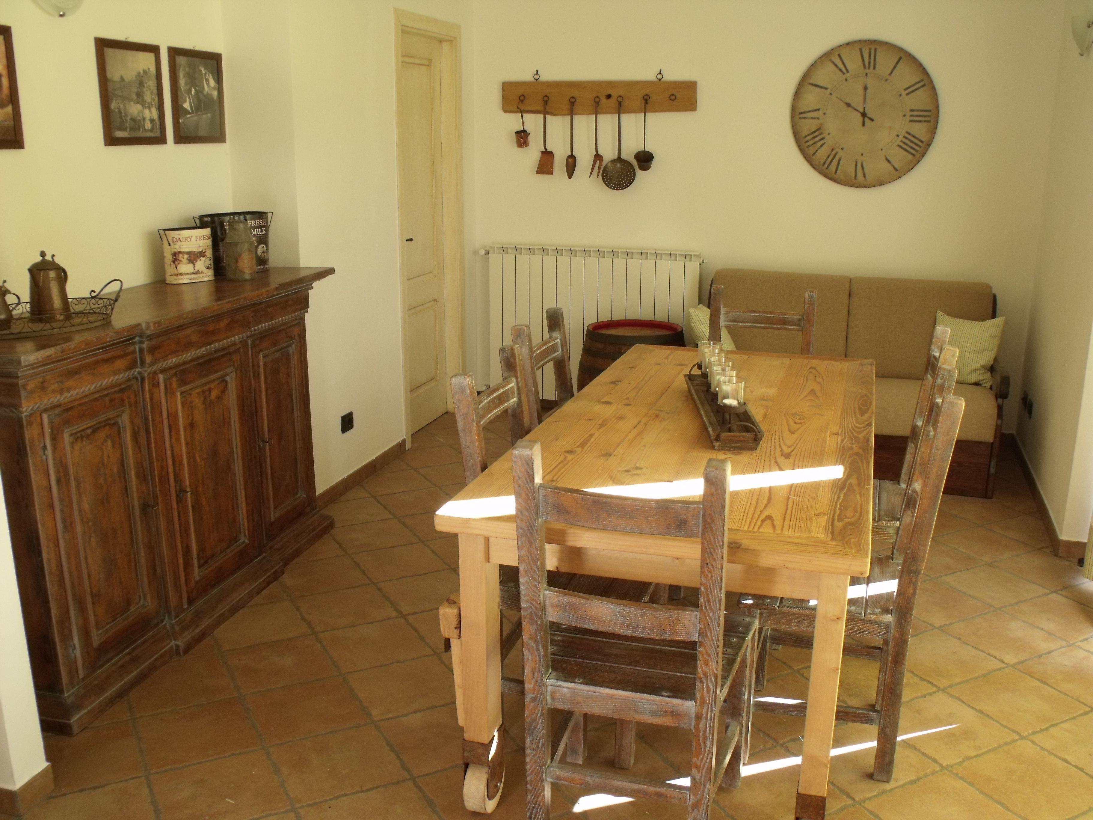 Uma área de refeições com mesa e cadeiras de madeira, um relógio na parede e um radiador acima da mesa.