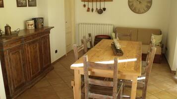 Uma área de refeições com mesa e cadeiras de madeira, um relógio na parede e um radiador acima da mesa.